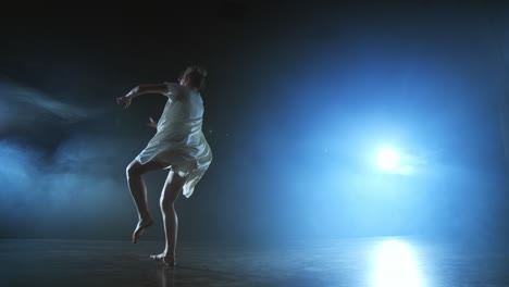 Una-Bailarina-Moderna-Con-Un-Vestido-Corto-Blanco-Realiza-Hermosas-Danzas-Dramáticas-De-Plástico-Corriendo-Por-El-Escenario,-Cayendo-Al-Suelo-Y-Girando.-Linternas-Y-Humo.